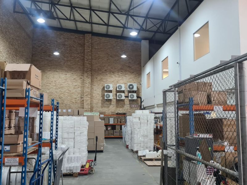Industrial warehouse space featuring high ceilings with exposed steel trusses, brick wall finishes, and multiple wall-mounted air conditioning units.