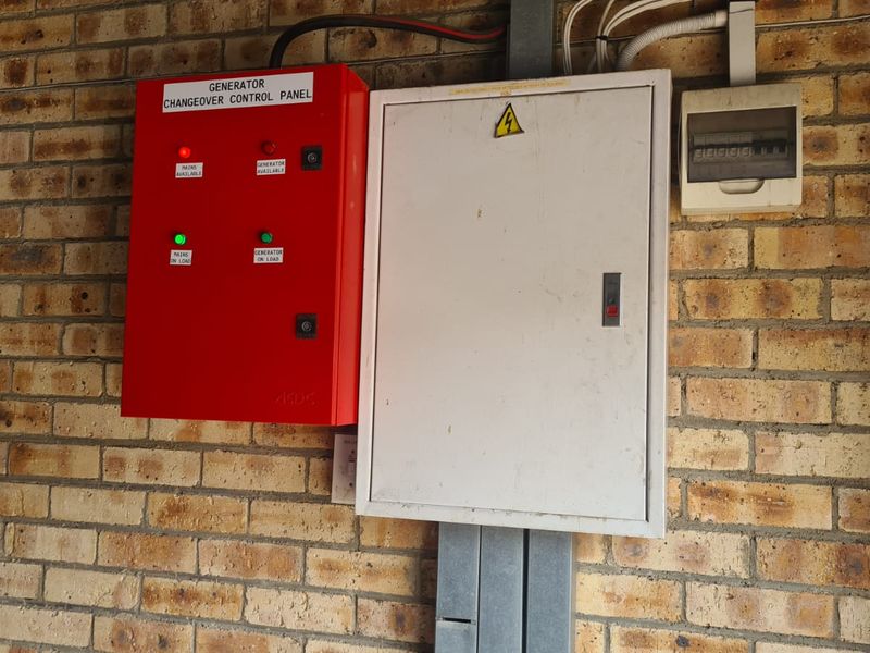 Industrial utility area featuring a wall-mounted generator changeover control panel and electrical distribution board on exposed brickwork.