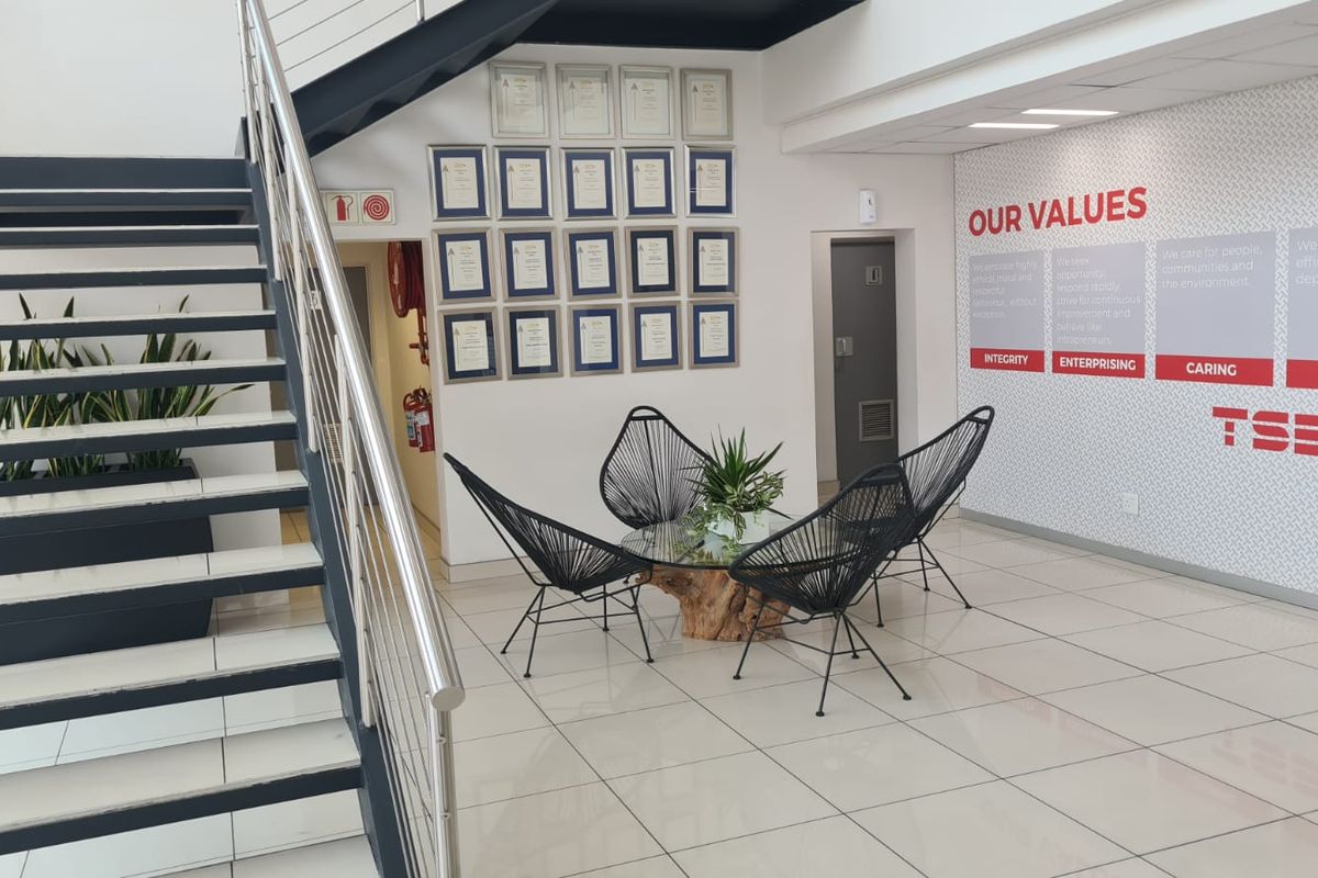 Modern industrial office entrance featuring a sleek metal staircase with stainless steel railings and polished tiled flooring.