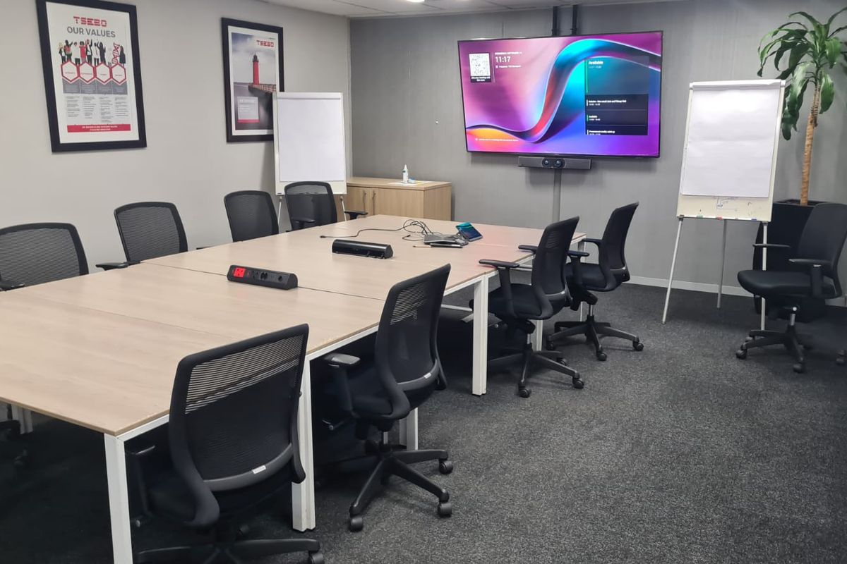 A professional boardroom or meeting room featuring a large wall-mounted display, integrated video conferencing technology, and neutral finishes.