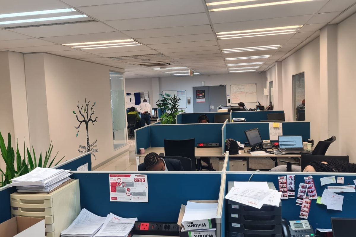 Open-plan office space featuring modular cubicle workstations, suspended ceiling with recessed lighting, and glass-partitioned office areas.