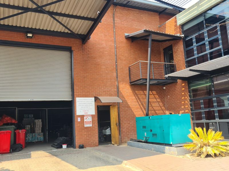 Industrial rear exterior featuring a large roller shutter door, brick facade, metal balcony, and an external backup generator.