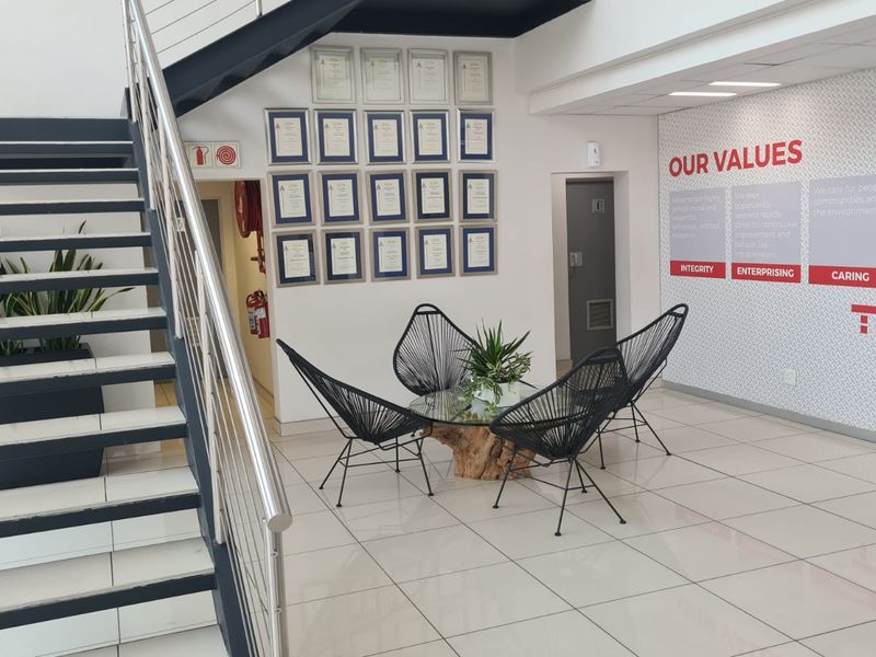 Modern industrial office entrance featuring a sleek metal staircase with stainless steel railings and polished tiled flooring.