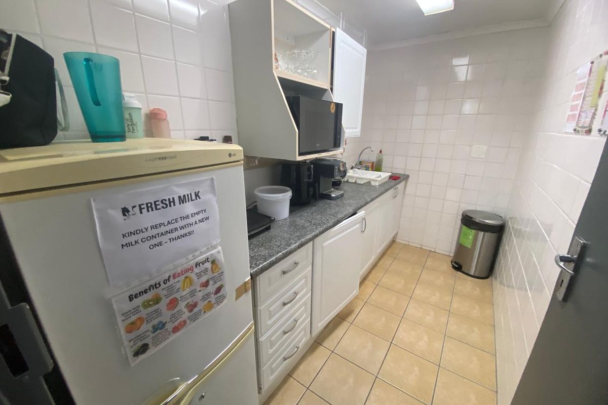 A functional kitchenette featuring tiled walls, laminate countertops, built-in cabinetry, and tiled flooring, suitable for office or staff utility use.