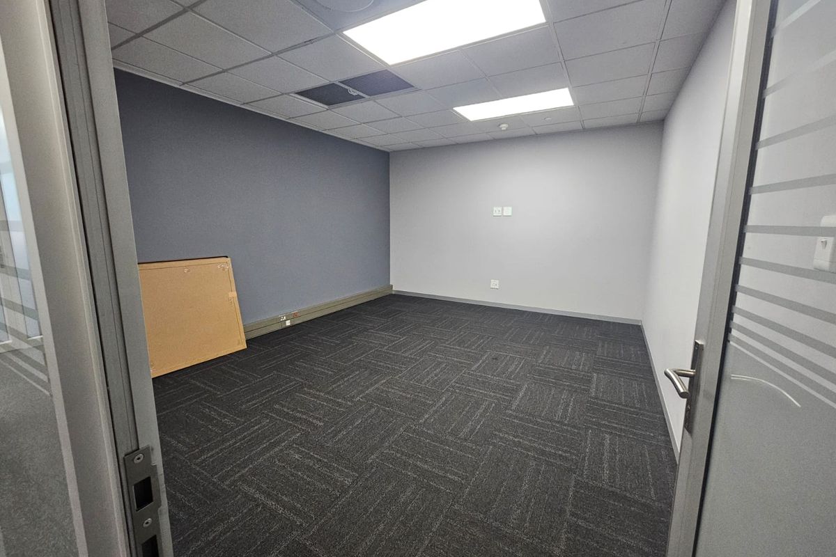 A clean, vacant office space featuring modern carpet tiles, a suspended ceiling with recessed lighting, and neutral wall finishes.