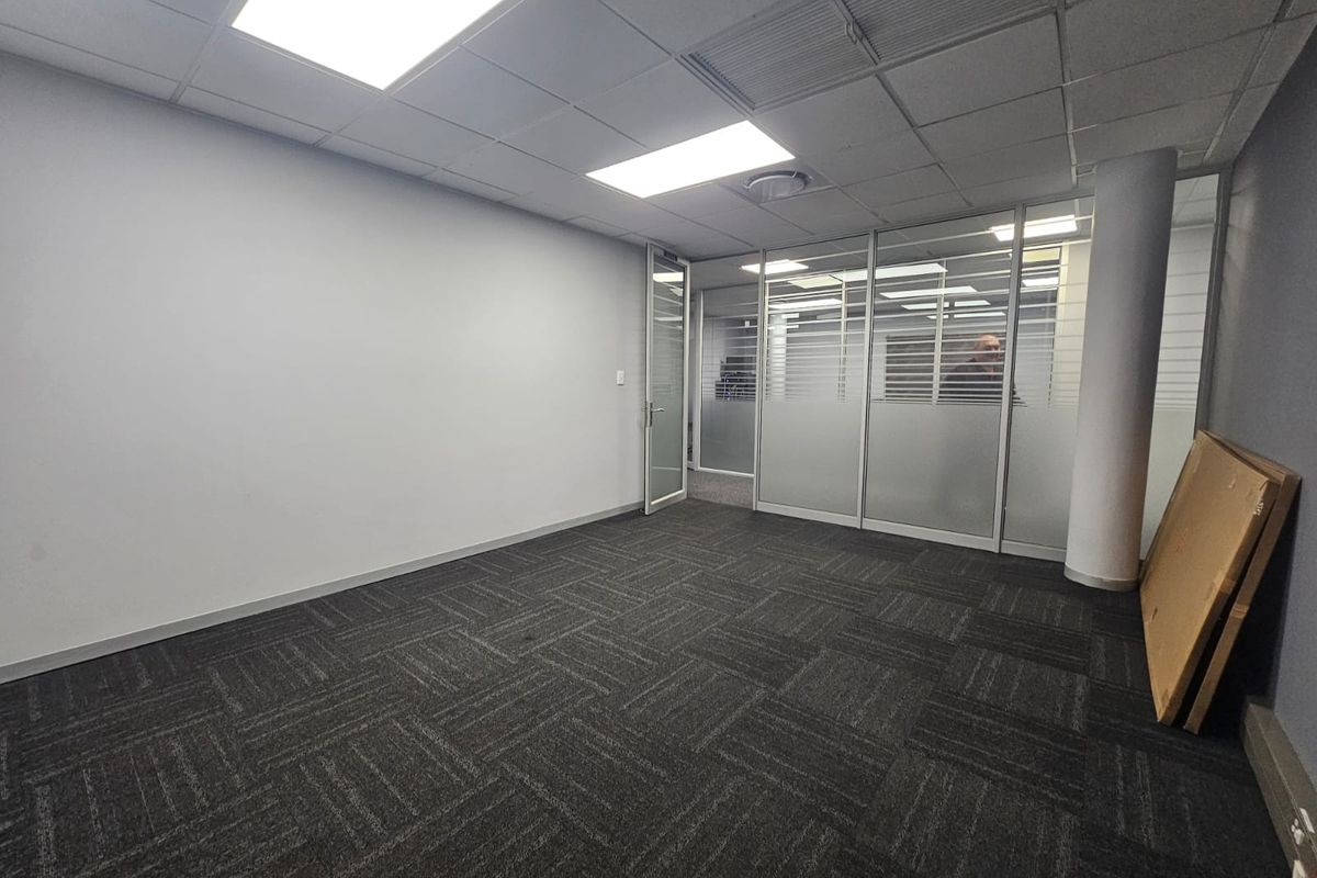 A vacant office space featuring carpeted flooring, a suspended ceiling with recessed lighting, and a modern glass partition wall.