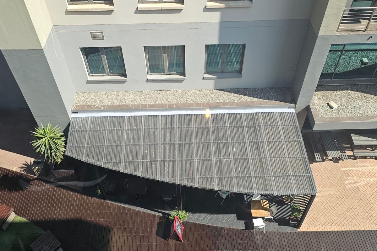 An aerial view of an office building exterior featuring a covered outdoor patio area with timber decking and a corrugated roof structure.