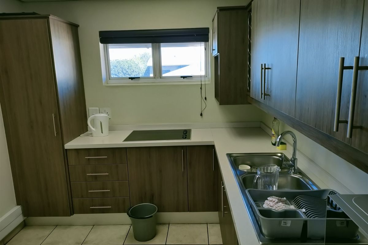 A functional kitchenette featuring wood-grain cabinetry, a built-in induction hob, a stainless steel double sink, and tiled flooring.