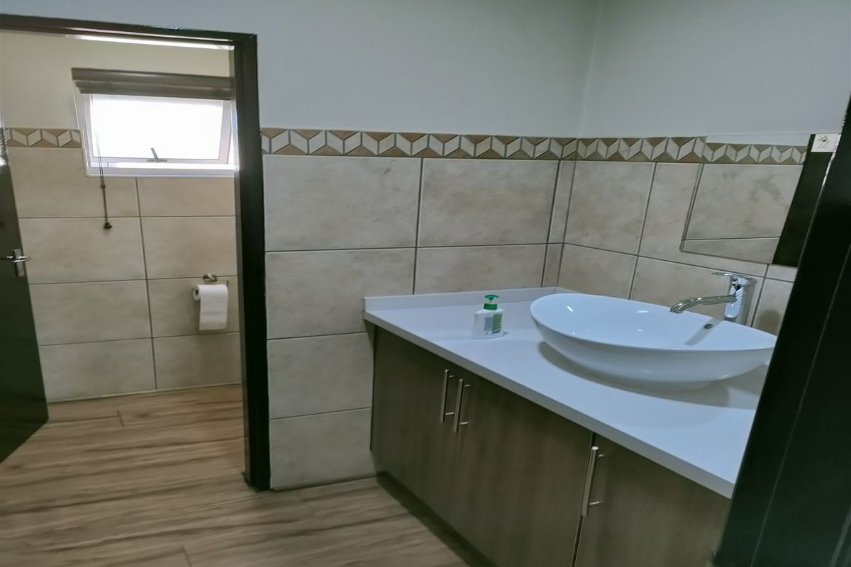 A functional bathroom featuring a modern vessel sink vanity, tiled walls with decorative border, and wood-look flooring, leading into a separate toilet area.