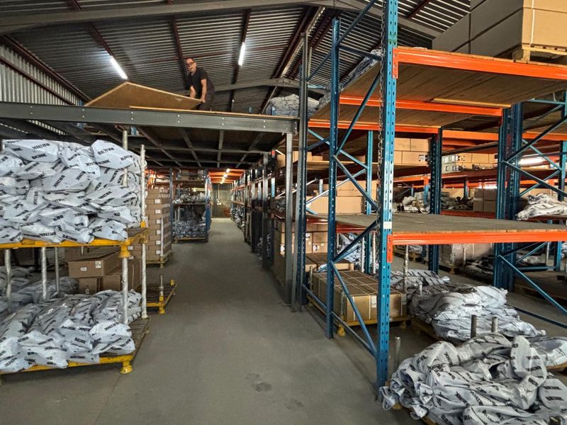 Industrial warehouse space featuring extensive steel racking systems, a mezzanine storage level, and exposed roof structure with concrete flooring.