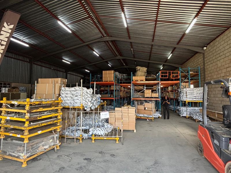 Spacious industrial warehouse featuring high corrugated metal ceilings, exposed steel trusses, durable concrete flooring, and extensive built-in industrial racking systems.