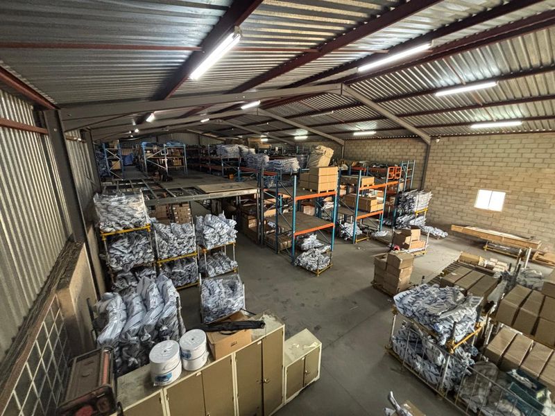 Spacious industrial warehouse featuring a steel portal frame, mezzanine storage level, concrete flooring, and high-bay fluorescent lighting, suitable for logistics or manufacturing operations.