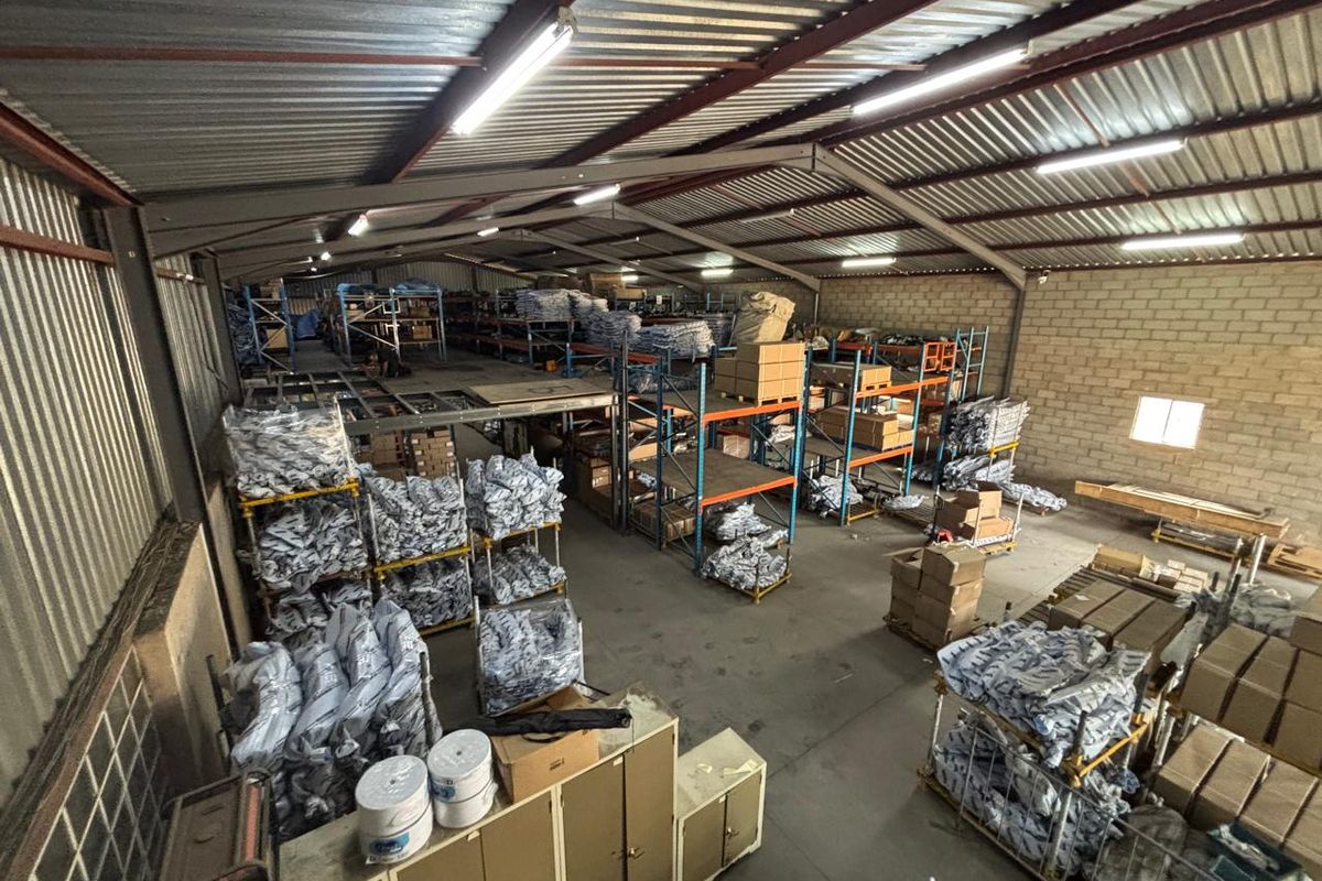 Spacious industrial warehouse featuring a steel portal frame, mezzanine storage level, concrete flooring, and high-bay fluorescent lighting, suitable for logistics or manufacturing operations.