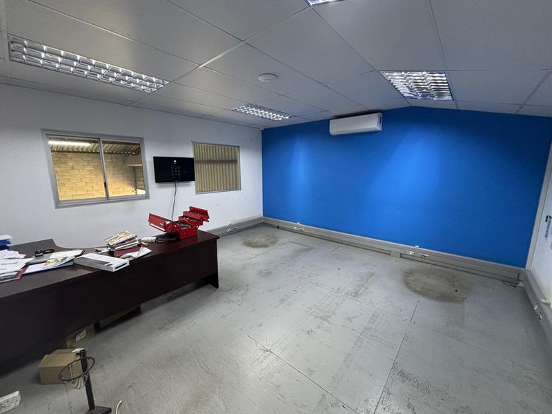 A functional industrial office space featuring a suspended ceiling, recessed lighting, split-system air conditioning, and durable painted concrete flooring.