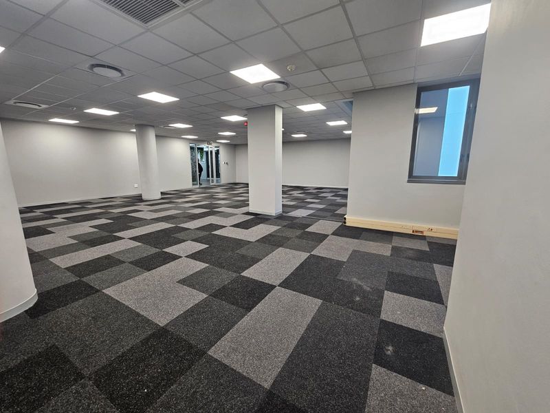 Spacious open-plan office area featuring modern carpet tiles, recessed ceiling lighting, and structural columns, providing a clean and professional workspace.