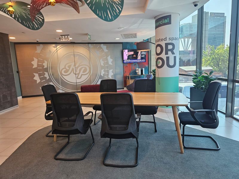 A modern, well-lit office meeting area featuring large floor-to-ceiling windows, tiled flooring, and integrated ceiling lighting within a professional commercial workspace.