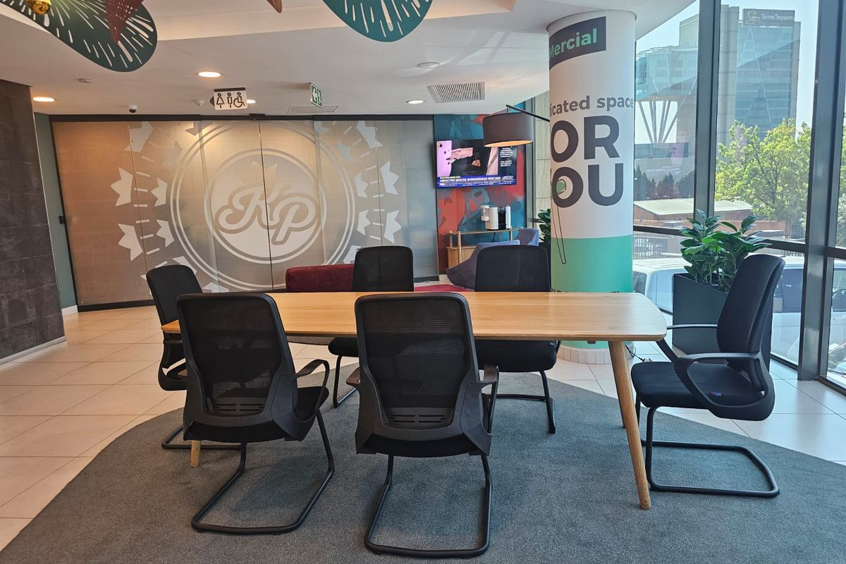 A modern, well-lit office meeting area featuring large floor-to-ceiling windows, tiled flooring, and integrated ceiling lighting within a professional commercial workspace.