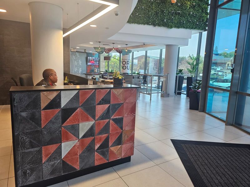 Modern office reception area featuring a decorative tiled desk, large floor-to-ceiling windows, and a green wall feature, providing a professional and welcoming entrance.