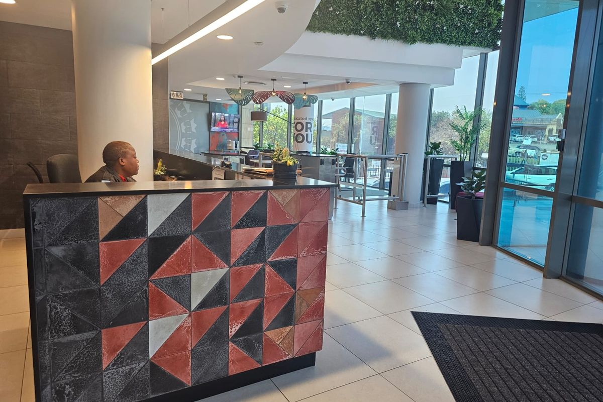 Modern office reception area featuring a decorative tiled desk, large floor-to-ceiling windows, and a green wall feature, providing a professional and welcoming entrance.