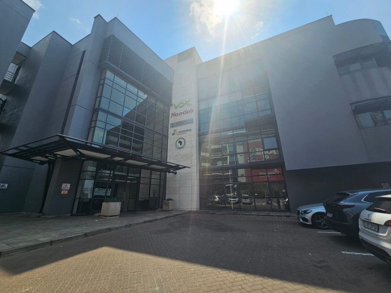 Modern multi-story commercial office building featuring a glass facade, metal entrance canopy, and paved parking area.