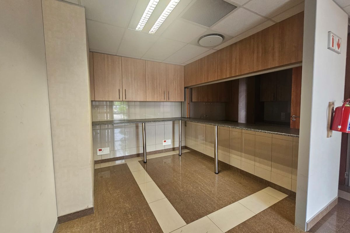 A clean, functional office kitchenette featuring built-in wooden cabinetry, granite countertops, tiled backsplash, and a drop ceiling with integrated lighting.