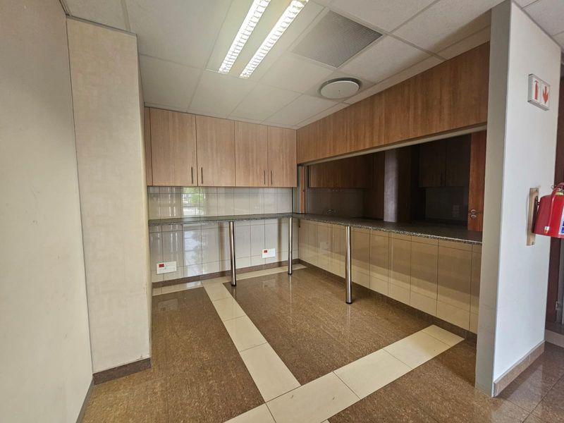 A clean, functional office kitchenette featuring built-in wooden cabinetry, granite countertops, tiled backsplash, and a drop ceiling with integrated lighting.