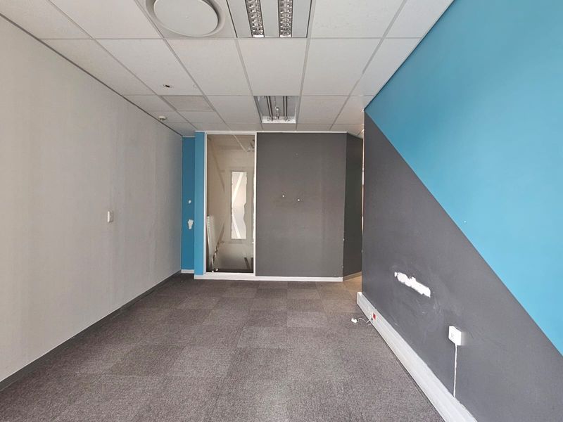 An empty office space featuring carpet tiles, a suspended ceiling with recessed lighting, and a glass partition wall, requiring minor cosmetic repairs.