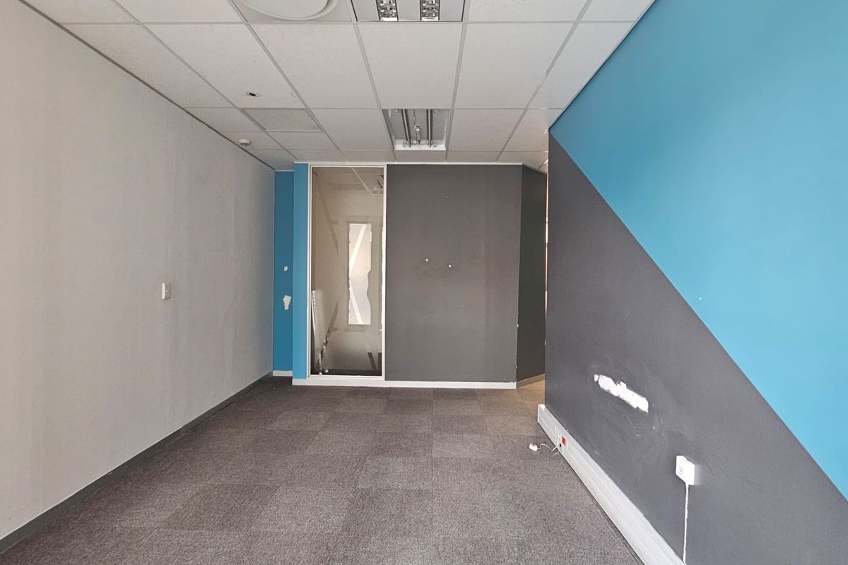 An empty office space featuring carpet tiles, a suspended ceiling with recessed lighting, and a glass partition wall, requiring minor cosmetic repairs.
