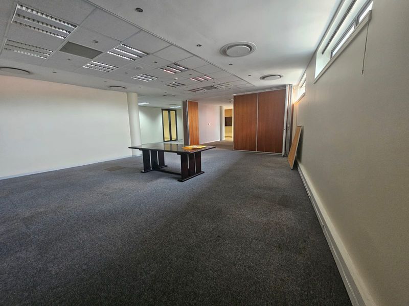 Spacious open-plan office area featuring suspended ceilings, recessed lighting, carpeted flooring, and a functional sliding partition wall for flexible space configuration.
