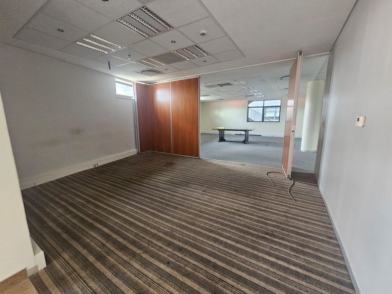 An empty office space featuring a flexible partition wall, suspended ceiling with recessed lighting, and carpeted flooring.