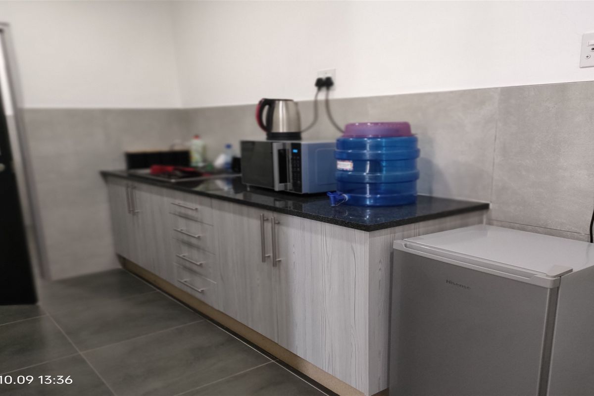 A compact kitchenette area featuring modern grey cabinetry, a dark stone countertop, and large format floor tiles.