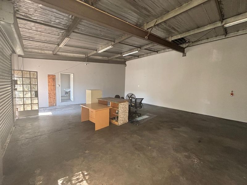 Open-plan industrial utility space featuring exposed steel beams, concrete flooring, and direct access to a small internal washroom area.