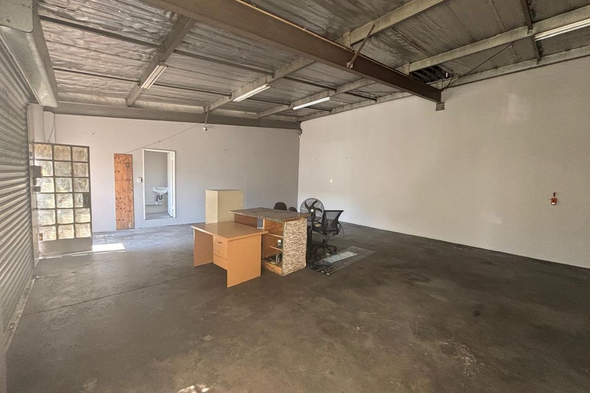 Open-plan industrial utility space featuring exposed steel beams, concrete flooring, and direct access to a small internal washroom area.