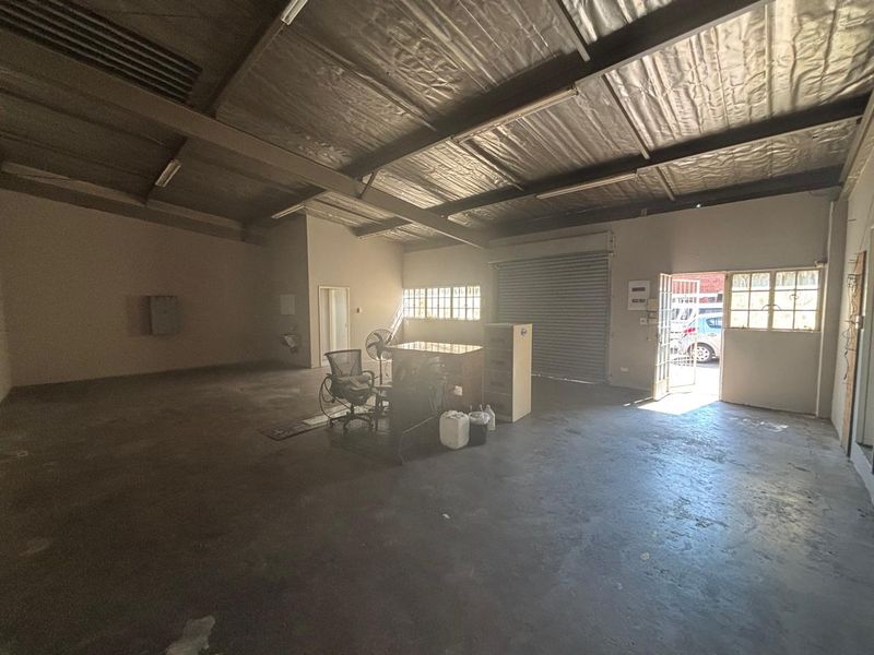 Spacious industrial utility area featuring exposed steel roof trusses, concrete flooring, and a large roller shutter door for convenient access.