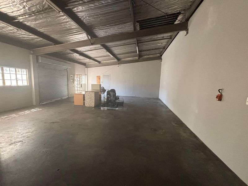 Spacious industrial utility area featuring exposed steel roof structure, concrete flooring, and a large roller shutter door, suitable for various commercial or storage uses.