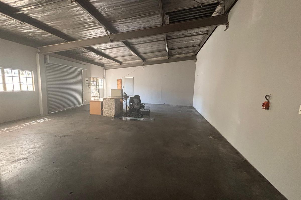 Spacious industrial utility area featuring exposed steel roof structure, concrete flooring, and a large roller shutter door, suitable for various commercial or storage uses.