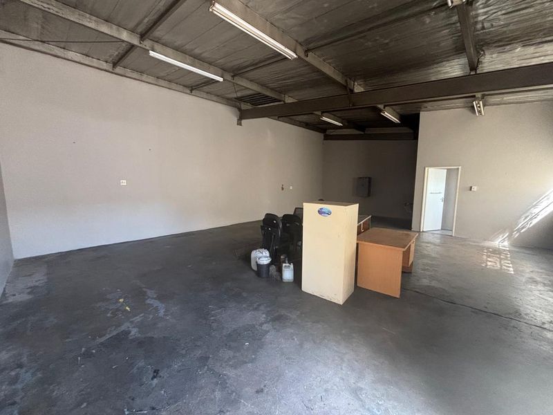 Spacious industrial utility area featuring exposed steel roof trusses, fluorescent lighting, and durable concrete flooring, suitable for various commercial or storage applications.