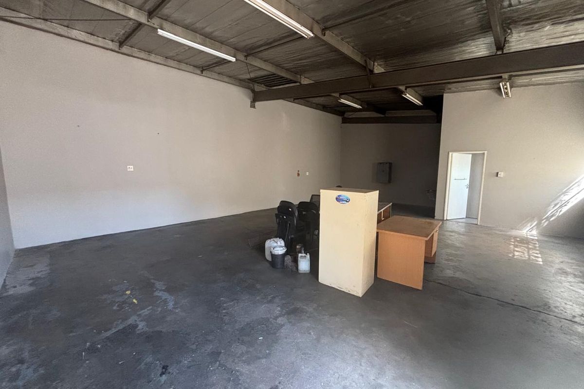 Spacious industrial utility area featuring exposed steel roof trusses, fluorescent lighting, and durable concrete flooring, suitable for various commercial or storage applications.