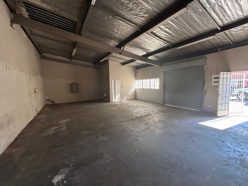 Spacious industrial utility space featuring concrete flooring, exposed steel beams, a large roller shutter door, and secure access gate.