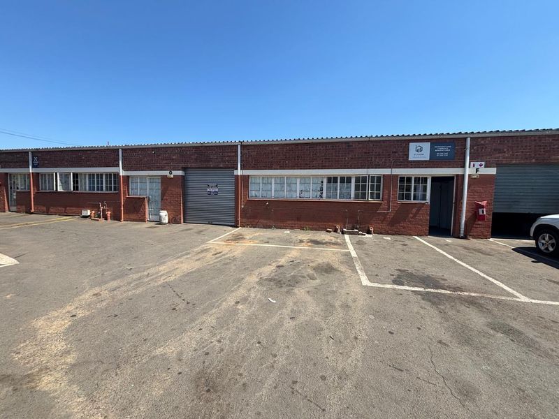 Front elevation of an industrial unit featuring exposed brickwork, steel-framed windows, and a roller shutter door with dedicated asphalt parking space.