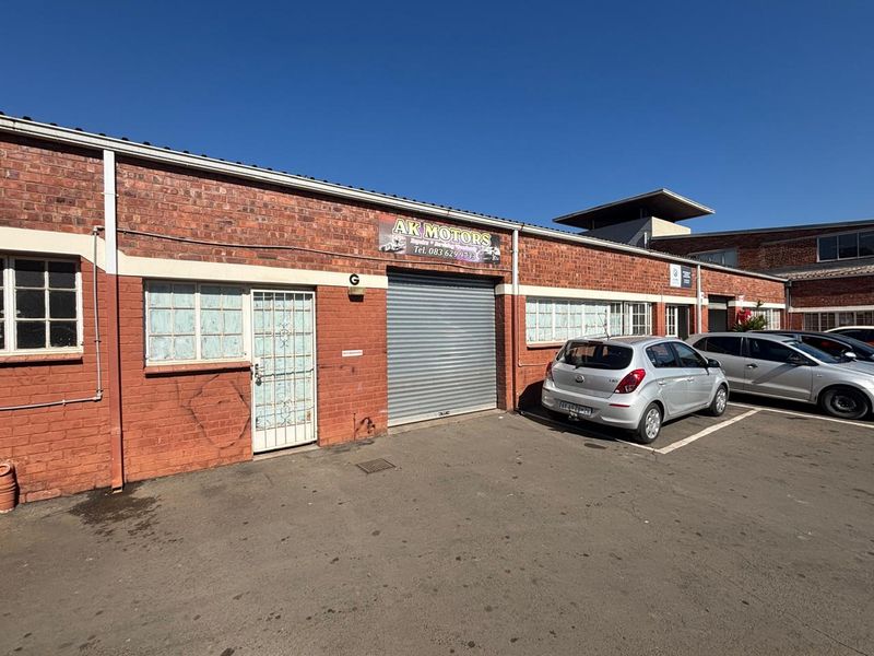 Industrial unit exterior featuring a red brick facade, roller shutter door, and dedicated parking space in a commercial complex.