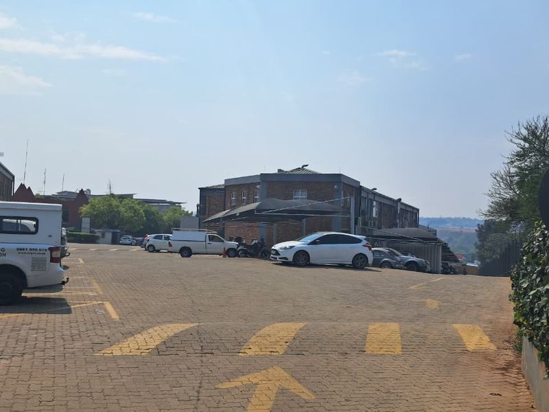 Exterior view of an industrial property featuring a paved parking lot with shade cloth carports and brick building structures.