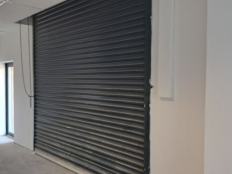 Industrial utility space featuring a secure roller shutter door, suspended ceiling, and concrete flooring, suitable for storage or workshop use.