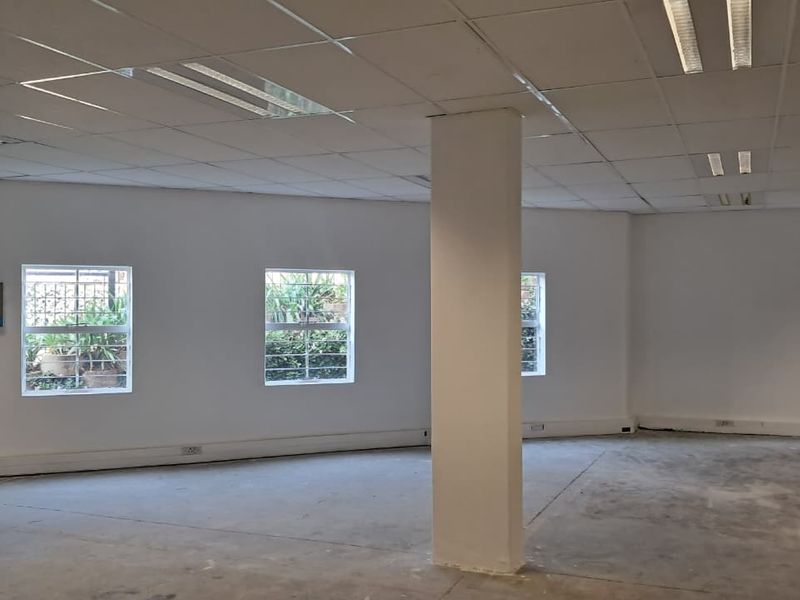 An open-plan industrial space featuring a suspended ceiling, structural column, and multiple windows with security bars, suitable for office or commercial use.