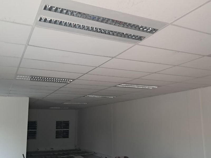 An empty industrial office space featuring a clean suspended ceiling with integrated recessed fluorescent lighting fixtures.