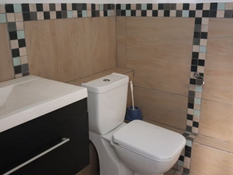 A functional bathroom featuring a modern vanity cabinet, ceramic basin, and toilet, finished with decorative tiled walls.