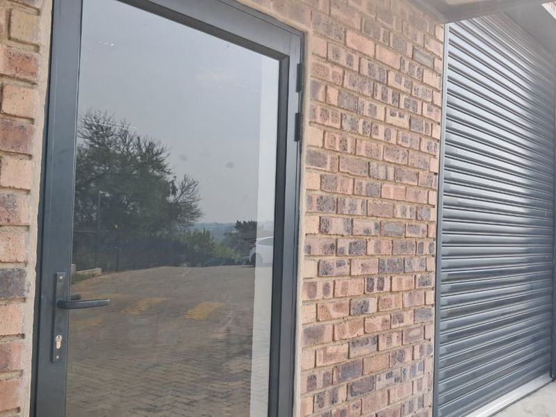 Exterior view of an industrial unit featuring a face brick facade, a secure glass entrance door, and a roller shutter door for vehicle access.