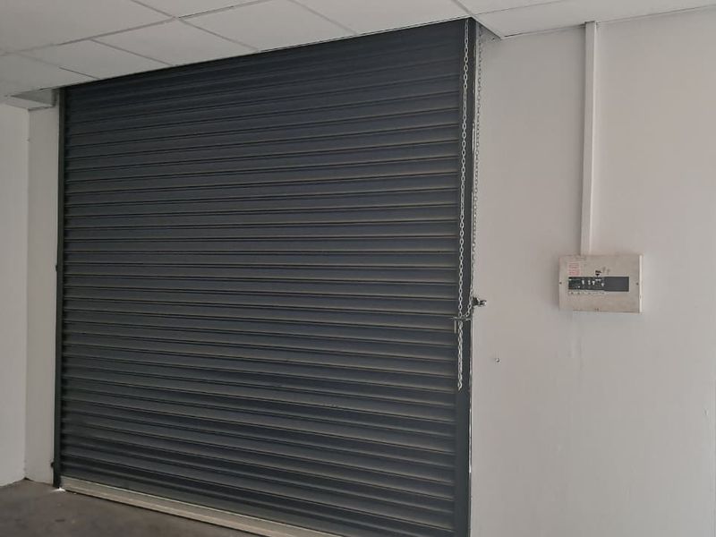 Industrial garage space featuring a secure roller shutter door, suspended ceiling, and an integrated electrical distribution board.