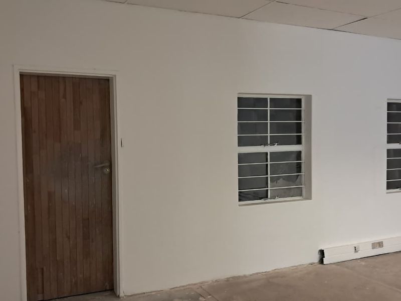 An empty industrial office space featuring white walls, a timber door, and windows fitted with security bars.