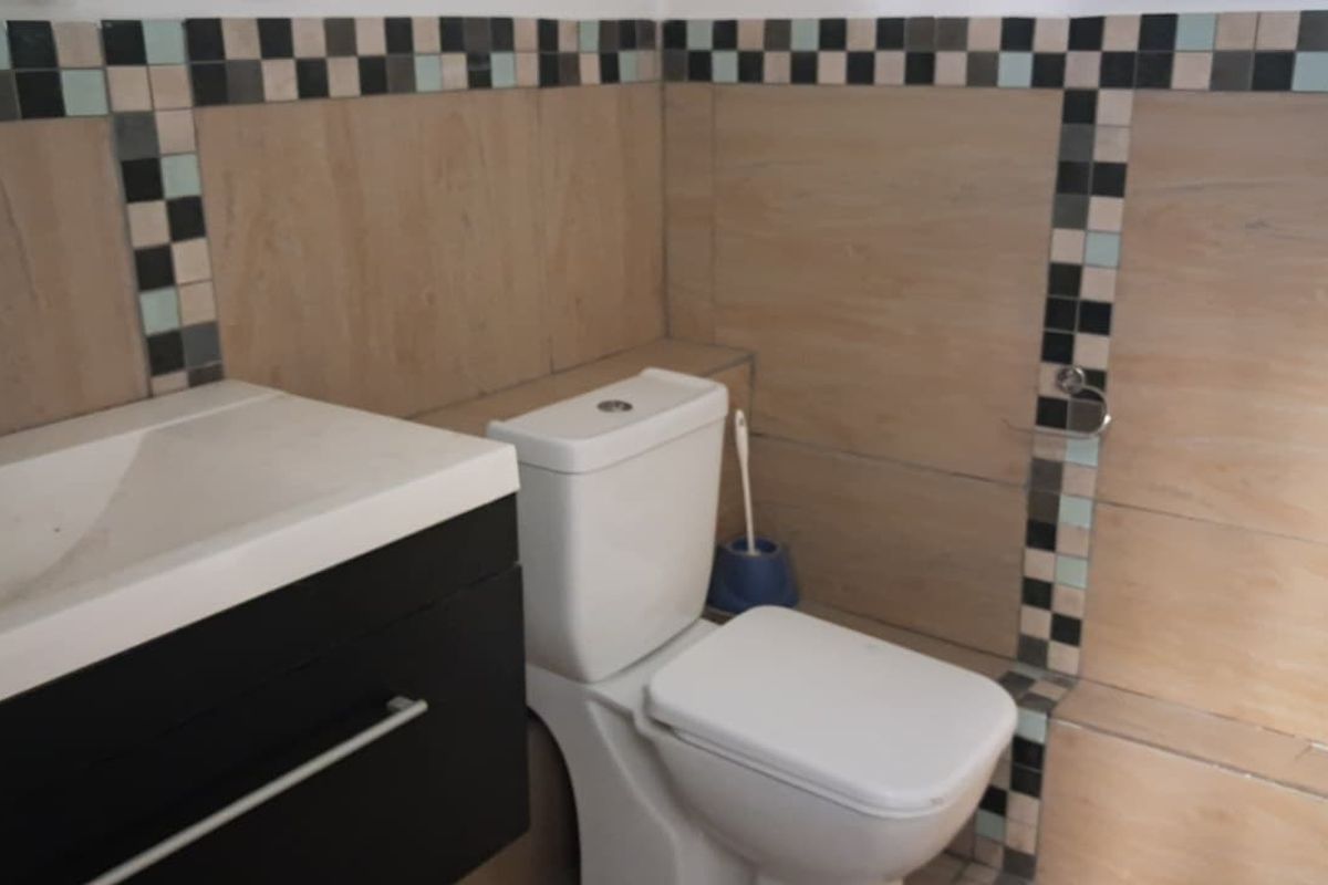 A functional bathroom featuring a modern vanity cabinet, ceramic basin, and toilet, finished with decorative tiled walls.